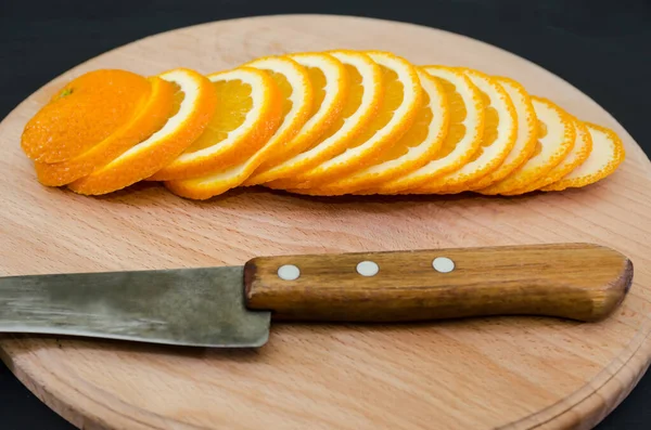 Sliced orange on a wooden board and knife. Close-up. Juicy orange slices on a blackboard.