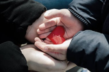 Kadın elleri bir çocuğun elini nazikçe tutar. Kırmızı kalp ellerinde. İki yerli insan arasındaki bakım, şefkat, bağlılık ve güven ifadesi. Resimler ayarlı.