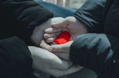 Kadın elleri bir çocuğun elini nazikçe tutar. Kırmızı kalp ellerinde. İki yerli insan arasındaki bakım, şefkat, bağlılık ve güven ifadesi. Resimler ayarlı.