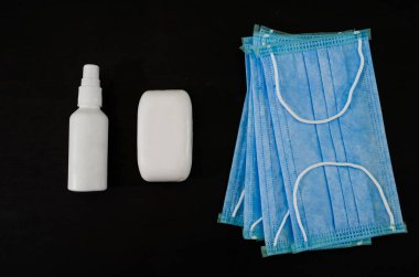 Koronavirüs enfeksiyonunun önlenmesi: el hijyeni için cerrahi maske, sabun ve el dezenfektanı. Siyah arka plan. Üst görünüm.
