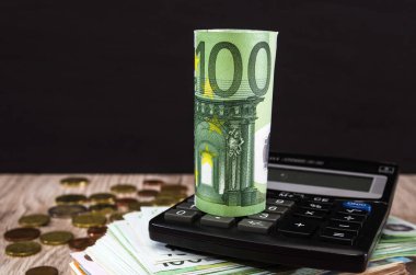 Hesap makinesiyle 100 Euro geldi. Ahşap arka plan, madeni paralar ve euro banknotu. İş konsepti.