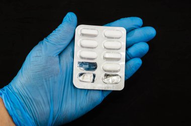 Mavi eldivenli bir el, siyah arka planda haplarla dolu bir su topladı. Yakın plan..