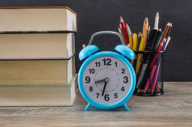 Masada yığınla kitap, mavi alarm saati ve renkli kalemler var. Eğitim kavramı.