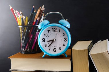 Bir yığın kitabın üzerinde mavi çalar saat ve renkli kalemler. Eğitim kavramı.