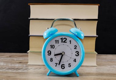 Kitapların arkaplanındaki mavi çalar saat. Eğitim konsepti. Dersleri öğrenme zamanı..
