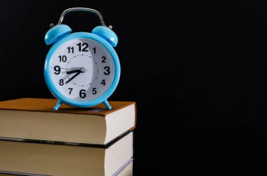 Bir yığın kitabın üzerindeki mavi çalar saat. Eğitim konsepti. Okula gitme zamanı. Mesaj için yer. Uzayı kopyala Siyah arkaplan.