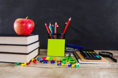 Bir yığın kitabın üzerinde elma, renkli kalemler ve ahşap bir arka planda okul malzemeleri. Eğitim kavramı.