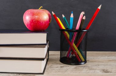 Bir yığın kitabın üzerinde elma ve tahta arka planda renkli kalemler. Eğitim kavramı.