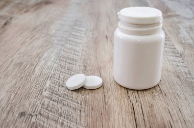 İki beyaz hap ve tahta arka planda bir kavanoz. Sağlık kavramı.