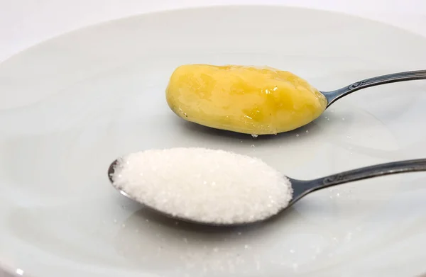 sugar and honey in spoons on white. The concept of choosing between sugar and honey.