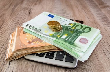 Bir hesap makinesinde yığınla bozuk para ve euro banknotları. Woody geçmişi. İş konsepti. Ekonomi ve tasarruf kavramı