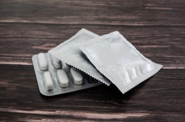 Prezervatif ve haplar ahşap bir arka planda su toplamış. Yakın plan. Doğum kontrol yöntemleri..