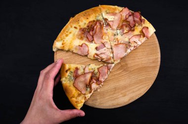 Eller bir dilim pizza alır. Siyah arka planda lezzetli bir pizza. Yukarıdan bak. Peynirli ve jambonlu pizza..