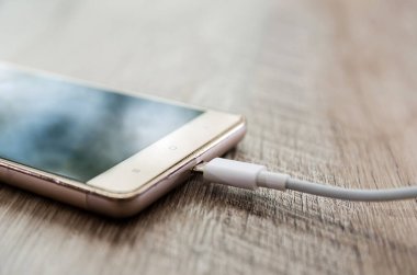 Telefondaki şarj aleti ahşap bir arka planda. Yakın plan. Akıllı telefon şarjı kavramı.