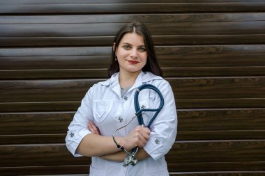 Beyazlı kadın doktor elinde steteskopla kameraya bakıyor. Ahşap arkaplan.