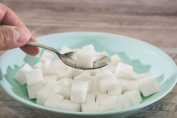 sugar cubes in a plate and spoon on a wooden background. Sugar harm concept. Eat sugar with a spoon.