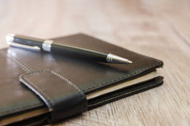 Siyah defter ve siyah kalem tahta bir masanın üzerinde. Yakın plan..