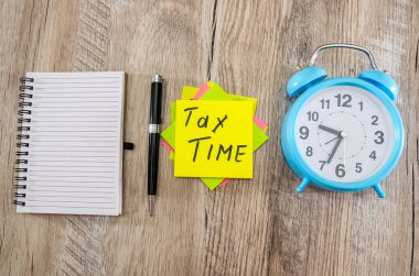 Vergi konsepti. Vergi zamanı. Yukarıdan bak. Mavi alarmlı saat, defter, çıkartmalar ve tahta bir masa üzerindeki kalem..