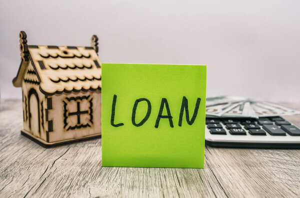 Концепция банковского кредита. Наклейка со словом "кредит", деньги, деревянный дом и калькулятор
.