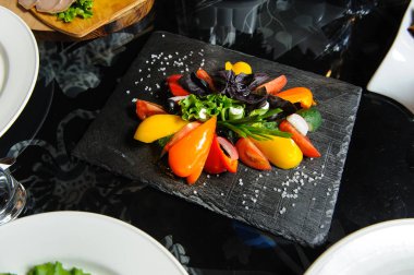 Restoranda tahta bir tahtanın üzerinde dilimlenmiş sebzeler, salatalıklar, domatesler, biberler, marul yaprakları.