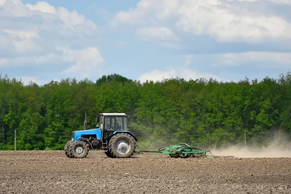 A blue tractor plows the field in the spring — Stock Photo, Image