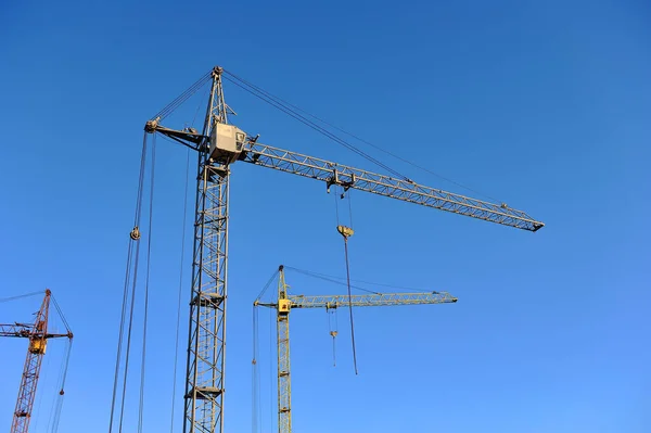 Três guindastes de construção contra o céu azul — Fotografia de Stock