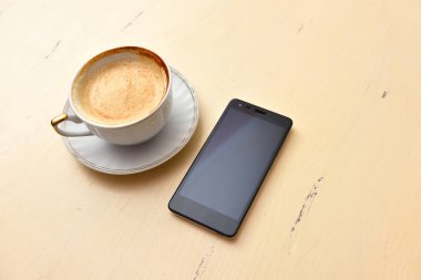 Eski bir masada cep telefonu ve kahve fincanı.