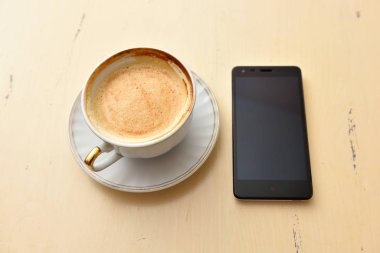 Eski bir masada cep telefonu ve kahve fincanı.