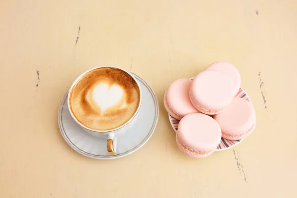 Cup of coffee with a pattern of hearts and macaroons on a vintage table — Stock Photo, Image