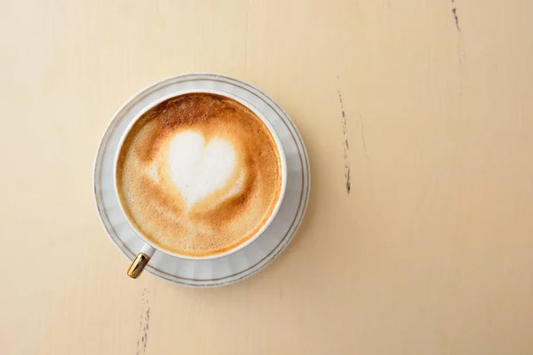 Uma xícara de café com um padrão de coração em uma mesa vintage — Fotografia de Stock