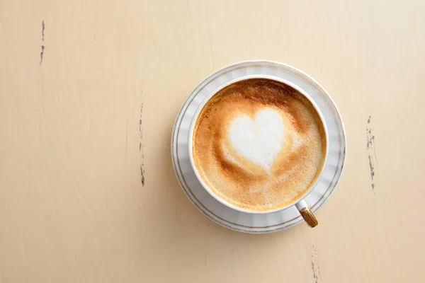 A cup of coffee with a heart pattern on a vintage table — Stock Photo, Image
