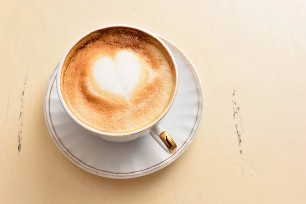 Uma xícara de café com um padrão de coração em uma mesa vintage — Fotografia de Stock