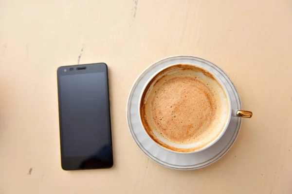 Telefone celular e xícara de café em uma mesa vintage — Fotografia de Stock