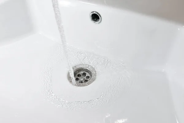 El agua fluye en un nuevo fregadero blanco en el baño —  Fotos de Stock