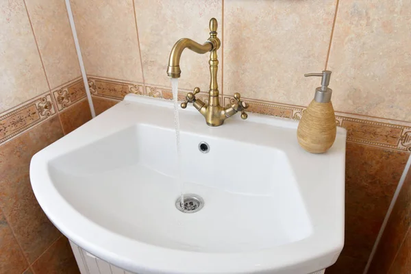 L'acqua scorre dal rubinetto di bronzo nel lavandino — Foto Stock