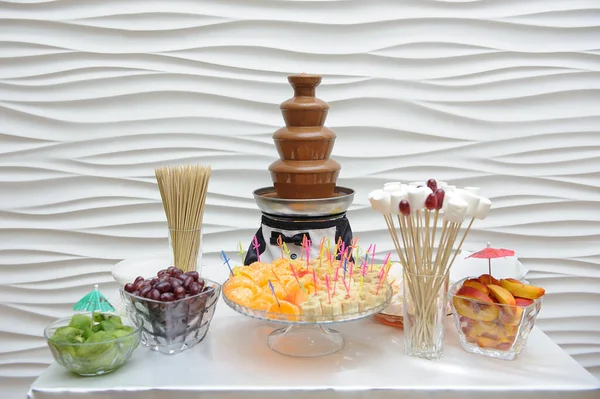 Schokoladenbrunnen und Tisch mit Obst auf weißem Wandhintergrund — Stockfoto