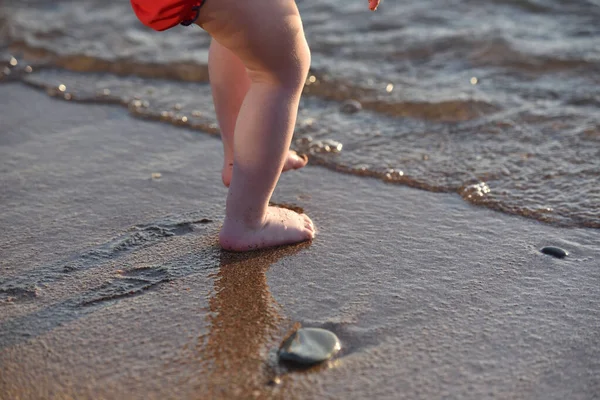 The feet of a small child on a sandy beach by the sea, he wants to enter the water — Stock Photo, Image