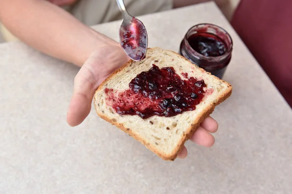 Borůvková marmeláda s lžící na kusu chleba, který leží v ruce — Stock fotografie