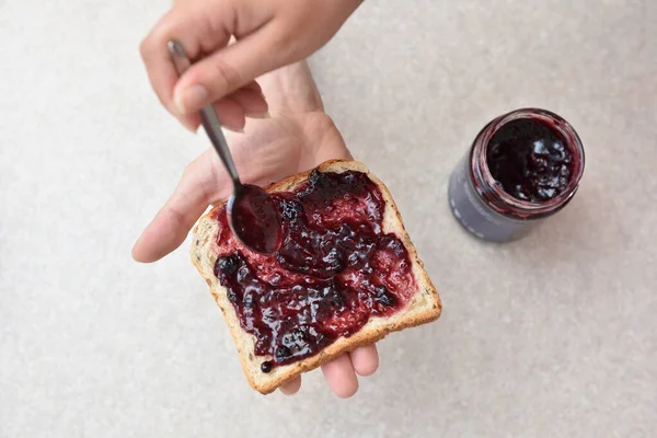 Borůvková marmeláda s lžící na kusu chleba, který leží v ruce — Stock fotografie