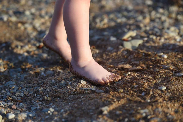 Die Beine eines kleinen Kindes. die Beine des Kindes gehen entlang eines Sandstrandes mit Kieselsteinen bis zum Meer — Stockfoto