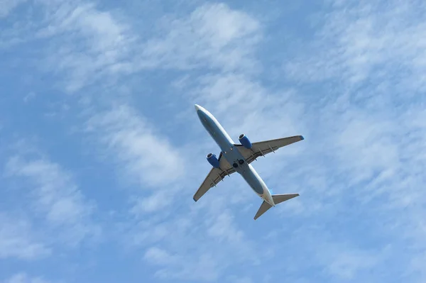 Het passagiersvliegtuig vliegt laag boven op een blauwe hemelse achtergrond. Onderaanzicht — Stockfoto