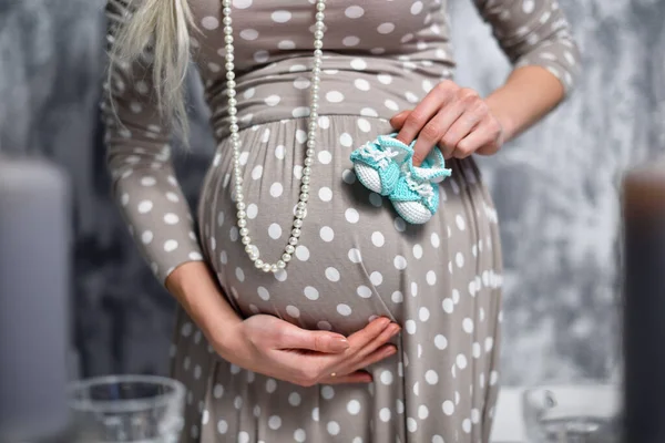 W ciąży dziewczyna trzyma jej brzuch i małe buty — Zdjęcie stockowe