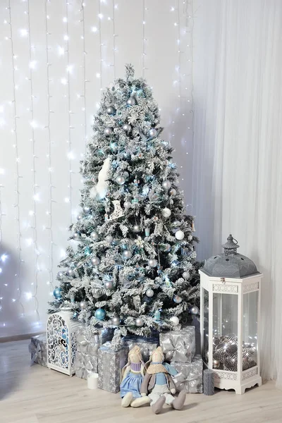 Nyårsinredning i en fotostudio i grått och vitt. En snövit julgran, presenter och lyktor, mot bakgrund av en vit vägg med en krans — Stockfoto