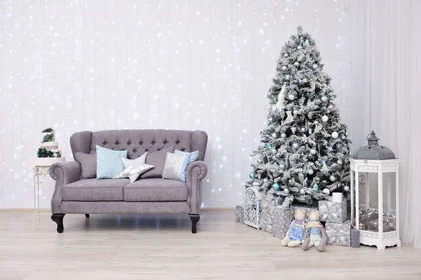 Nyårsinredning i en fotostudio i grått och vitt. Klassisk grå soffa med kuddar, snövita julgran, gåvor och en lykta, mot den vita väggen med en krans — Stockfoto