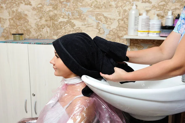 Девушка, сидящая в парикмахерской у стилиста, с перетасованной головой в полотенце после мытья волос — стоковое фото