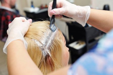 The hairdresser uses a brush to apply the dye to the hair, for d
