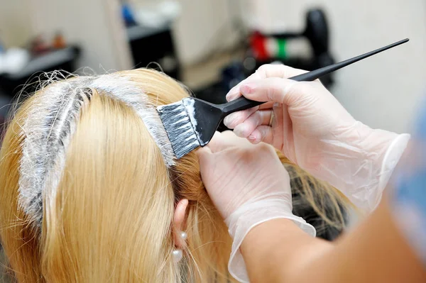 El peluquero utiliza un cepillo para aplicar el tinte en el cabello, para d — Foto de Stock