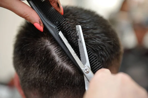 Парикмахер с ножницами и расческой стрижет волосы мужчине — стоковое фото