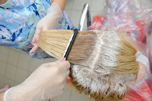 O cabeleireiro mancha a tinta em seu cabelo com um pente, para co — Fotografia de Stock