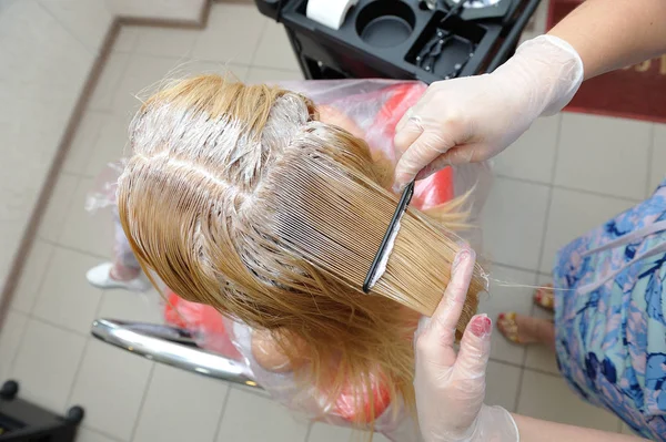 De kapper smeert de verf op zijn haar met een kam, voor co — Stockfoto